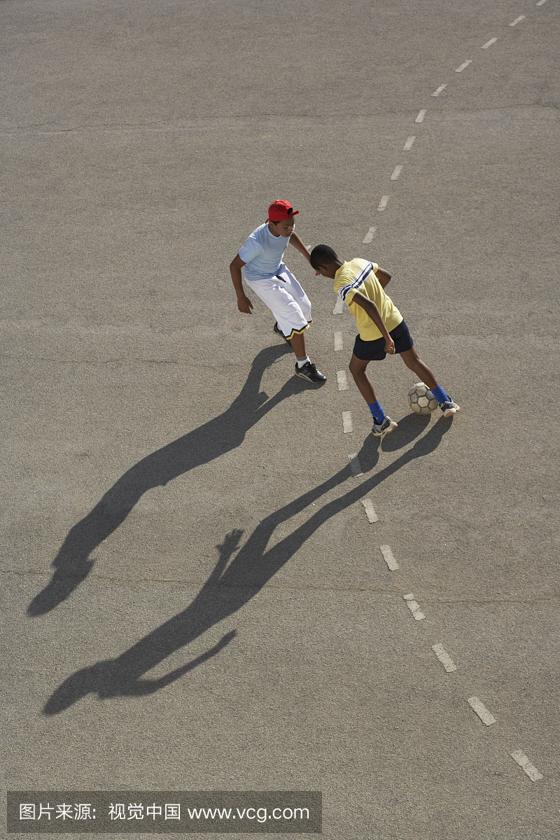 两个男孩(11-13岁)在沥青上踢足球,身高高高