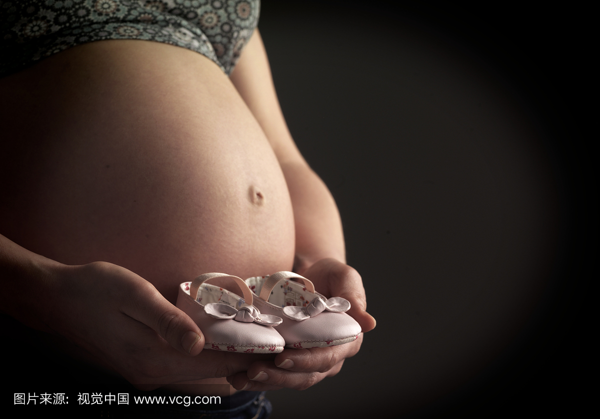 怀孕的女人抱着一双婴儿鞋,工作室拍摄,中段,关