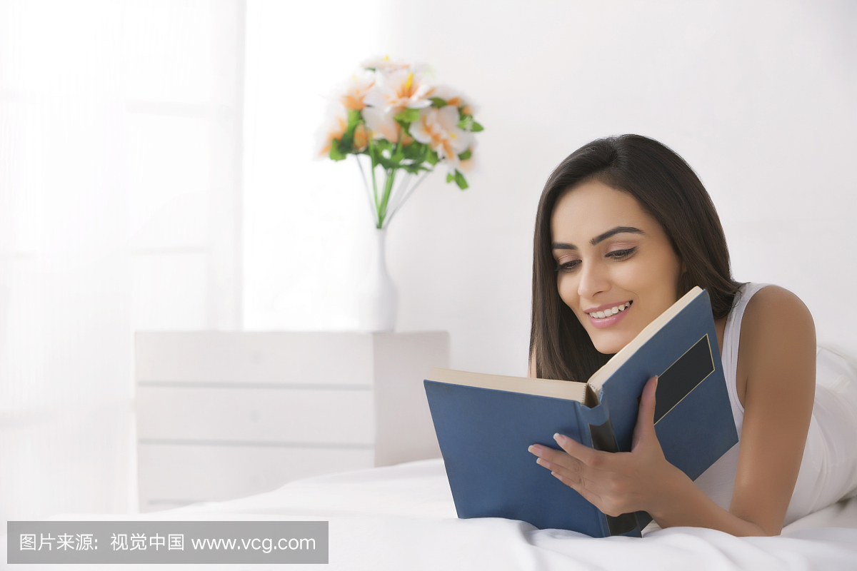 美丽的年轻印度女人在床上看书