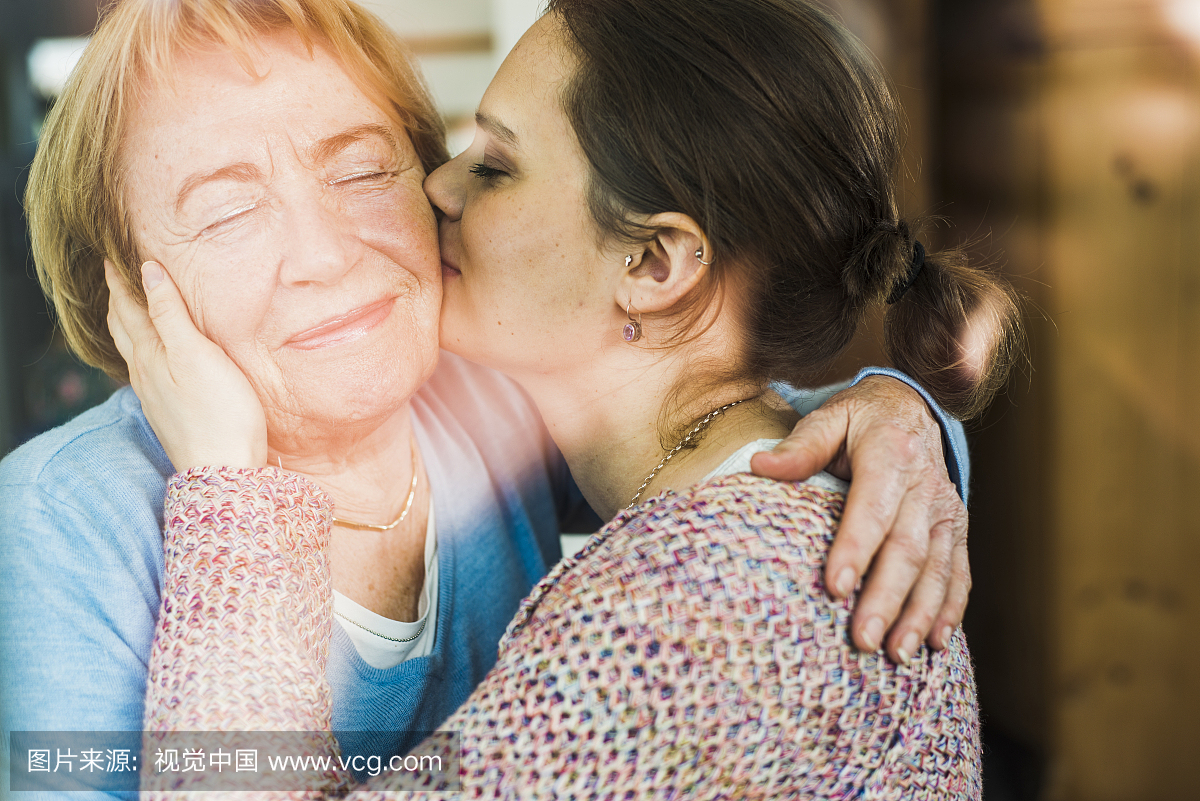 年轻女子亲吻高级妇女在窗玻璃后面