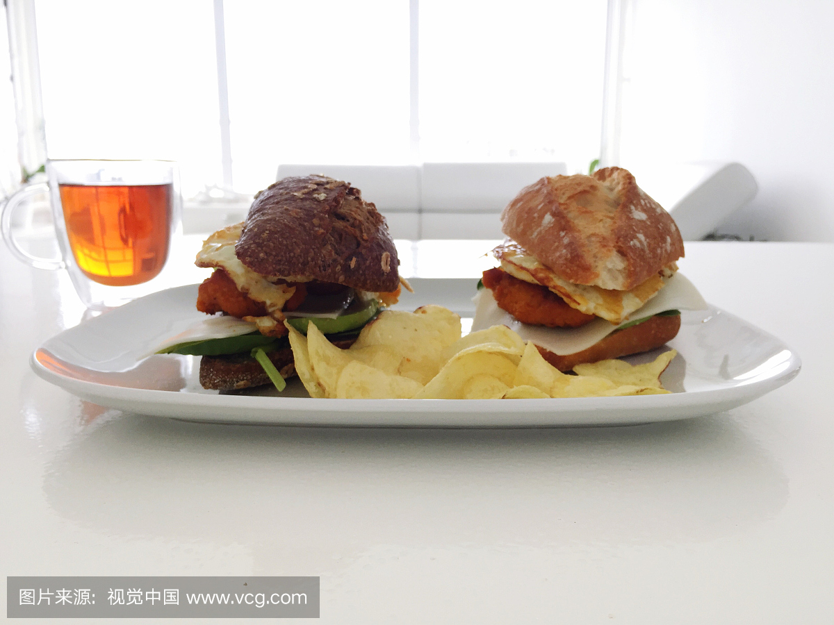 特写的新鲜汉堡和土豆片在板上与茶在桌子上