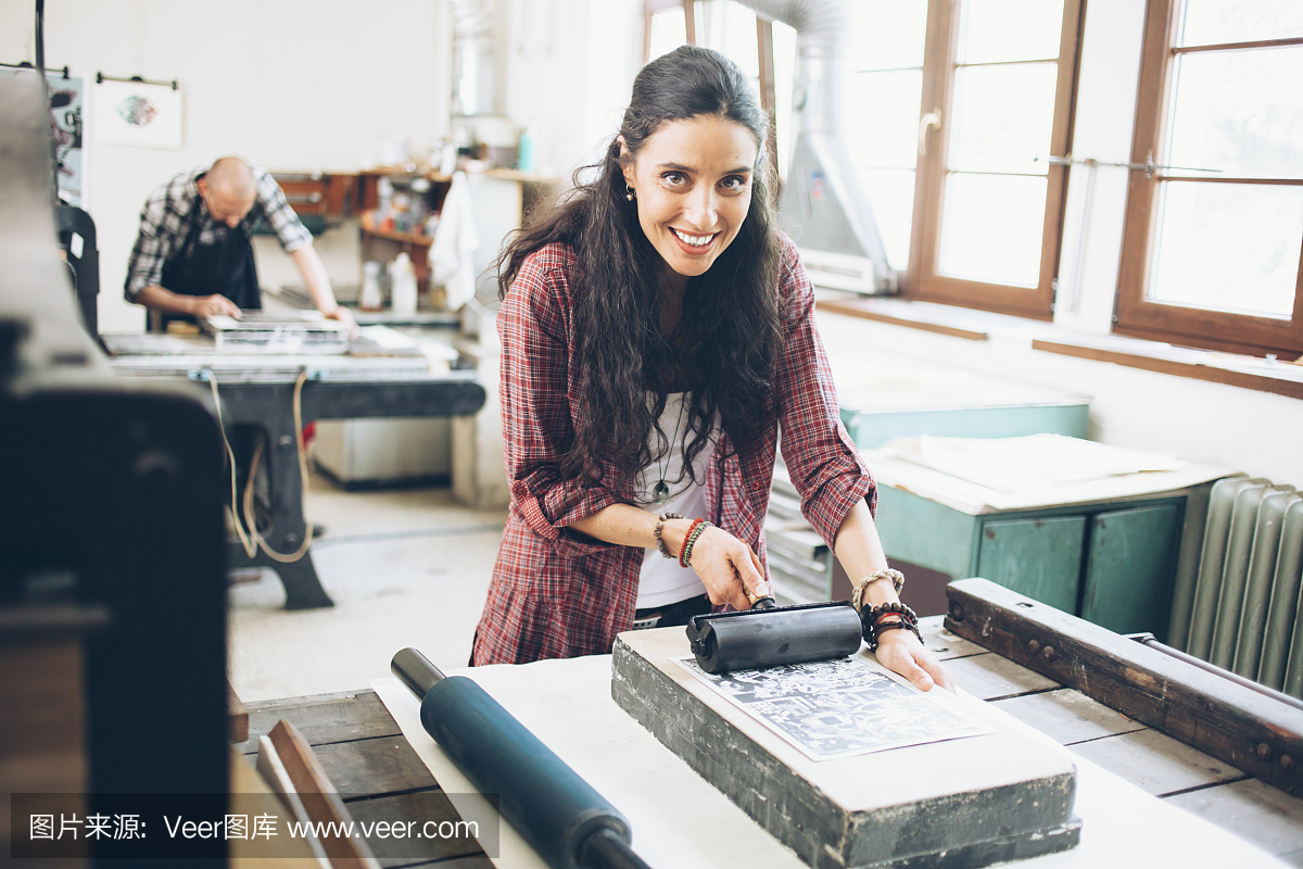 微笑的女性平版印刷工人在印刷厂使用滚筒