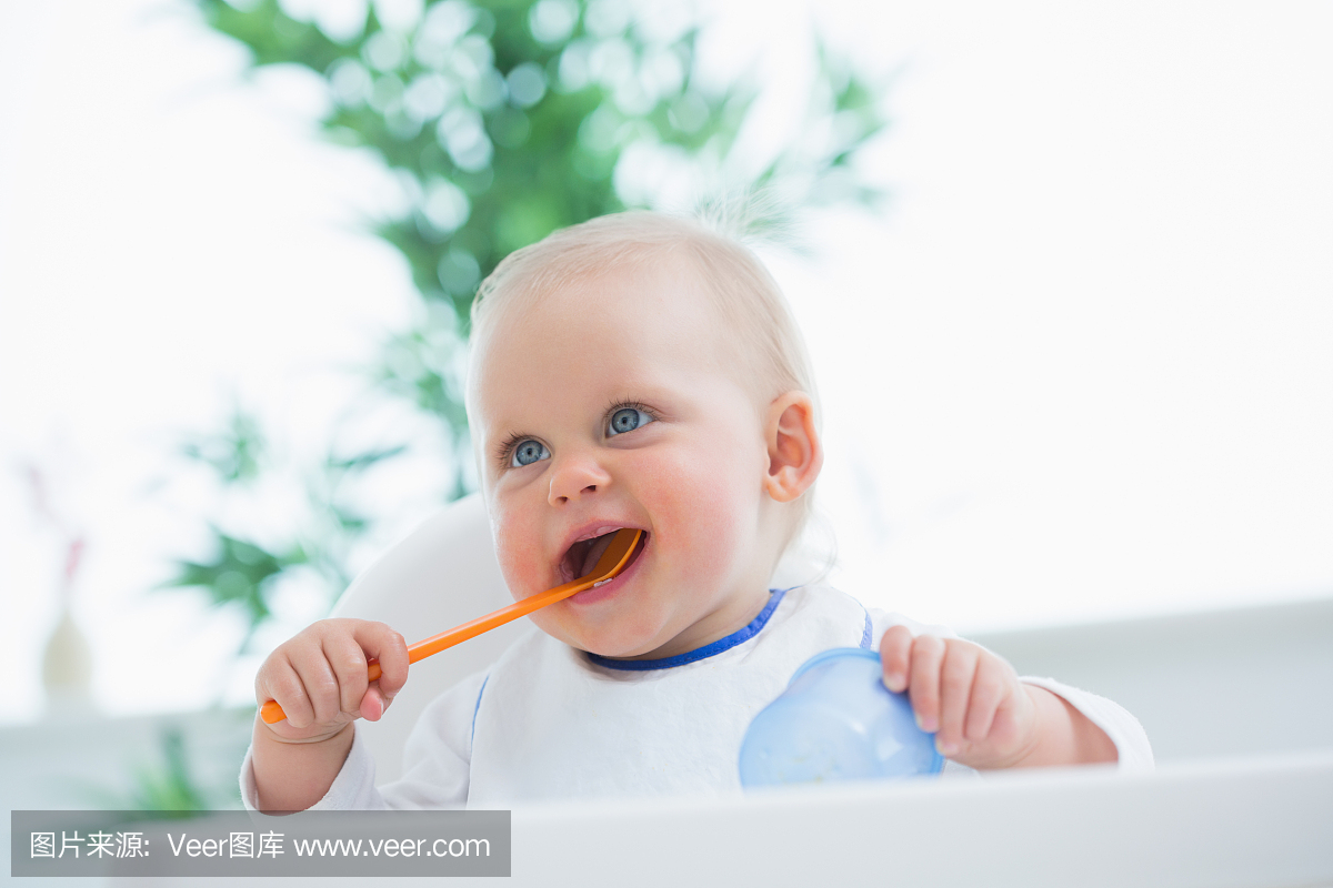 婴儿拿着勺子,而把它放在他的嘴里
