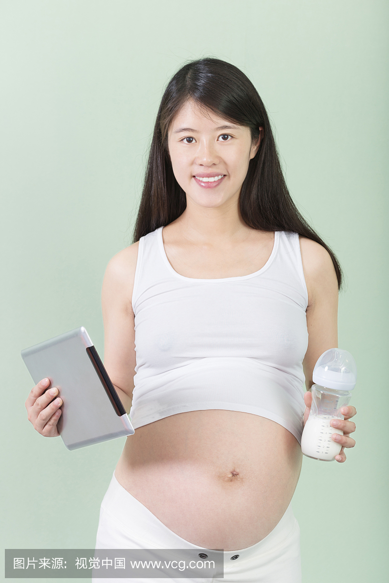 年轻美丽的孕妇站着露着大肚子拿着掌上电脑和