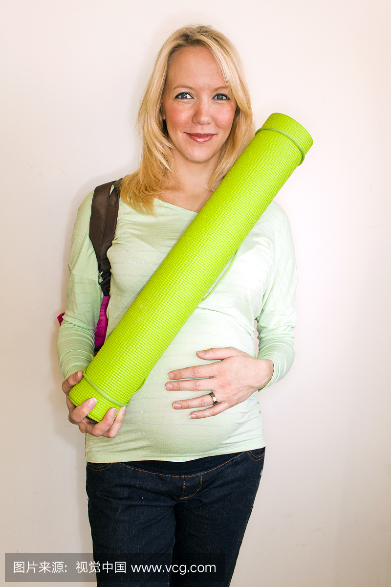 一个怀孕的女人拿着一个瑜伽垫里面。
