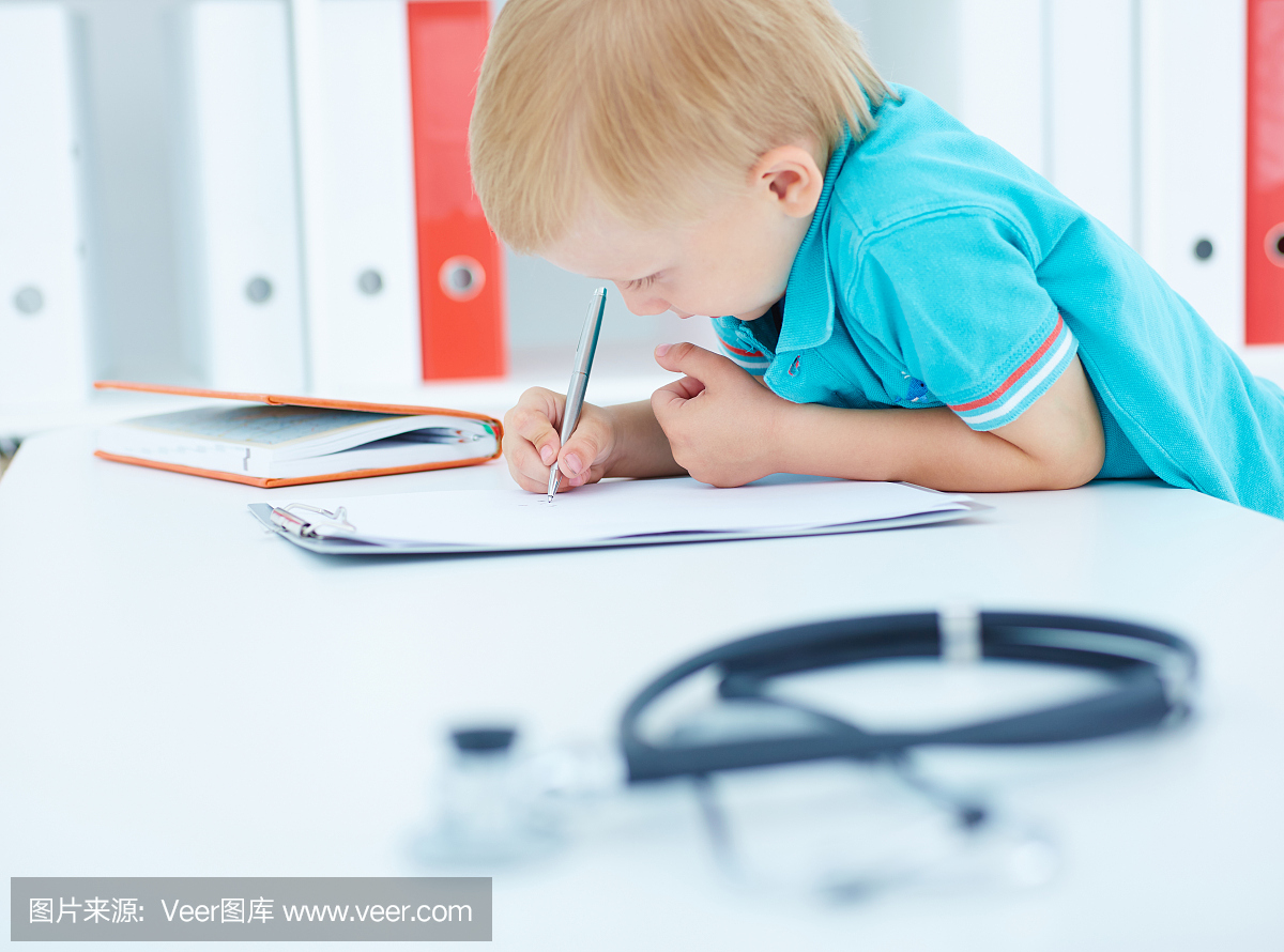 小男孩写在坐在医生的书桌上的剪贴板上。听诊