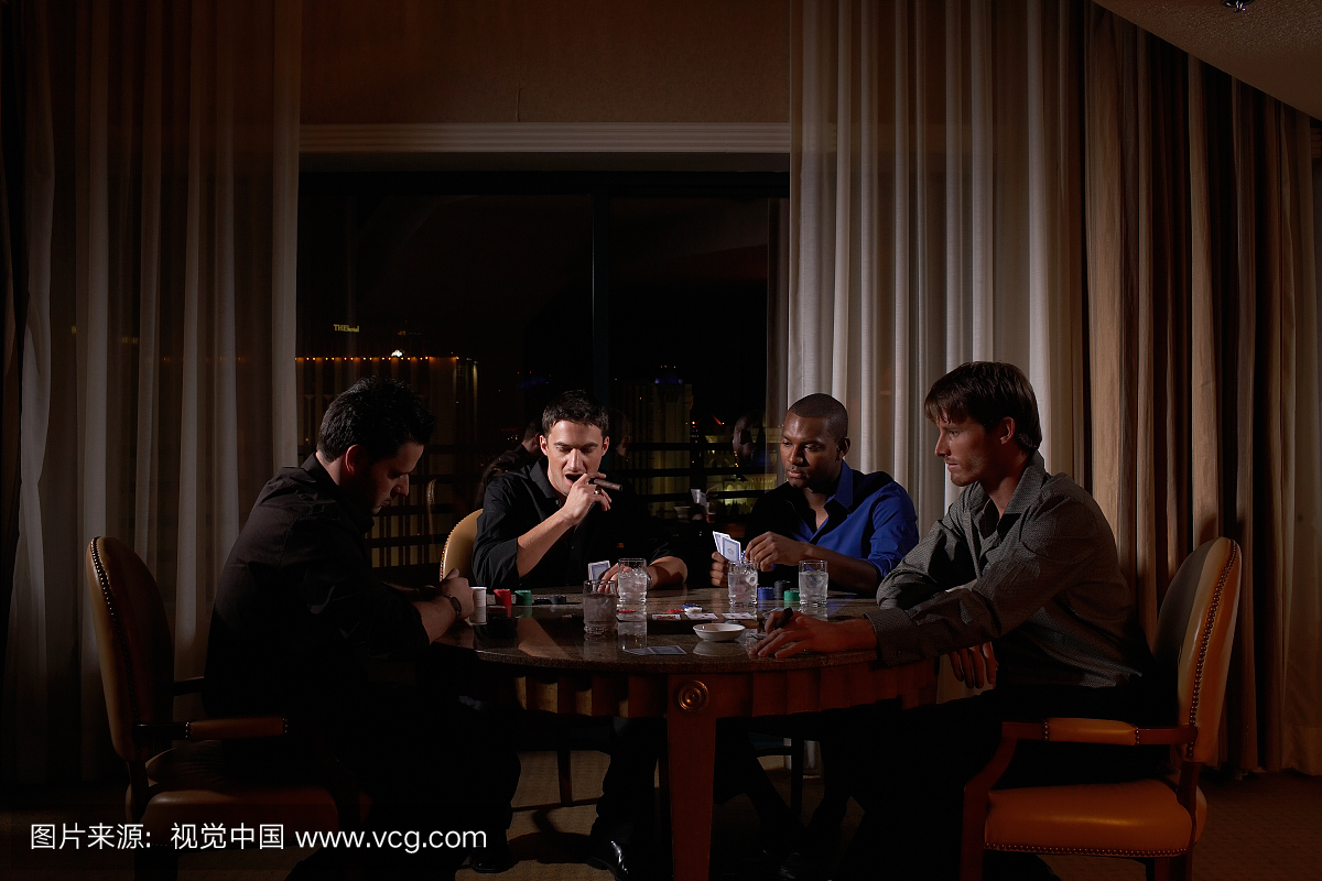 四人坐在圆桌上黑暗的酒店房间玩纸牌,一个吸