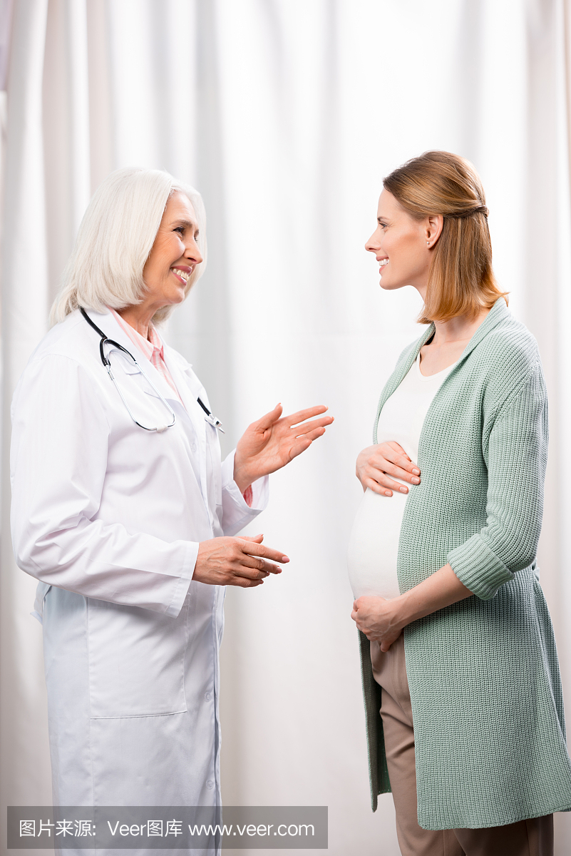 年轻孕妇与灰色头发医生在医疗咨询期间说话