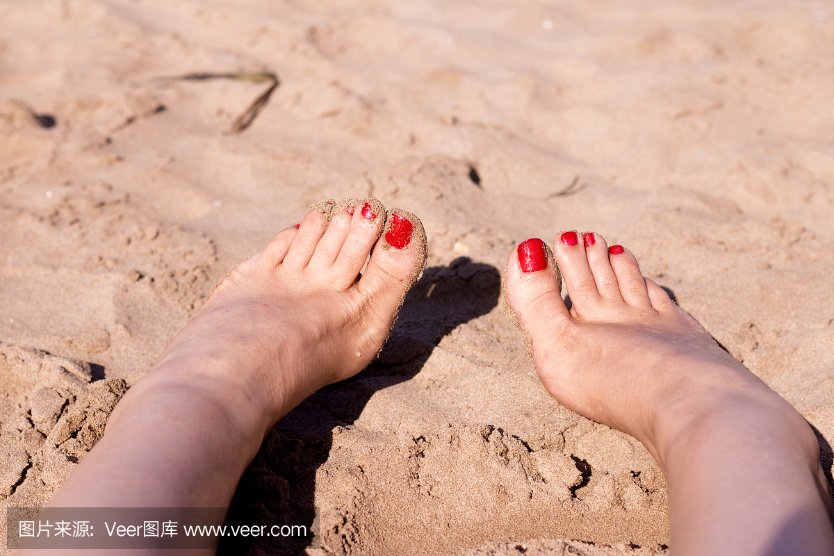 海滩场景与女人的脚在沙滩上。脚指甲涂成红色
