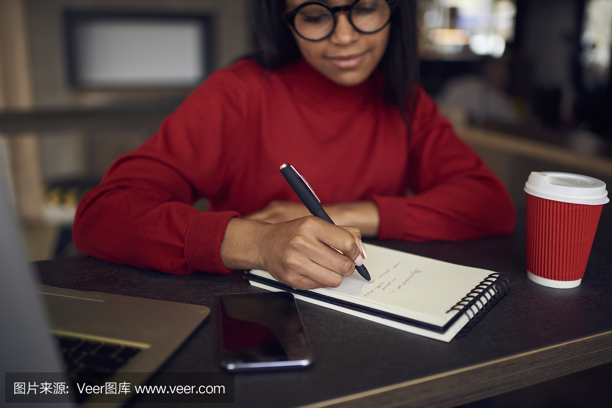 沉思的黑人美国学生在眼镜写日志的同时在咖啡