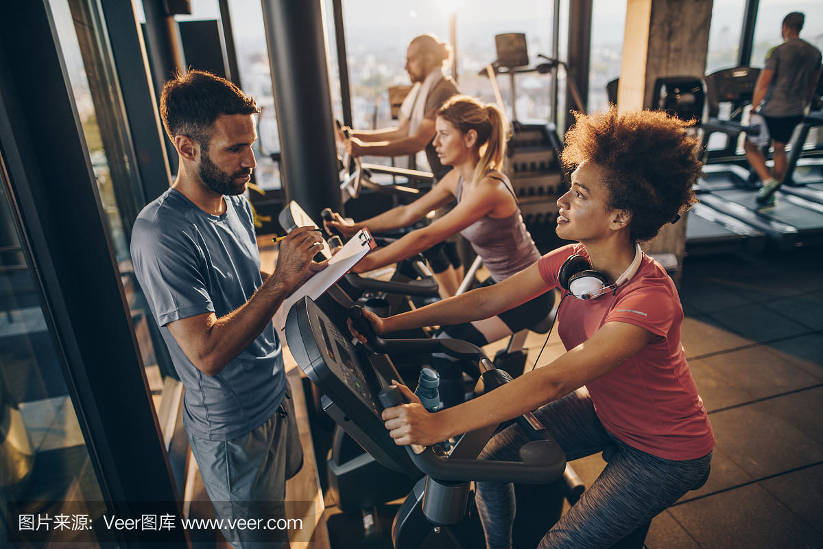 年轻的男教练在健身房纺织课程期间追踪运动员