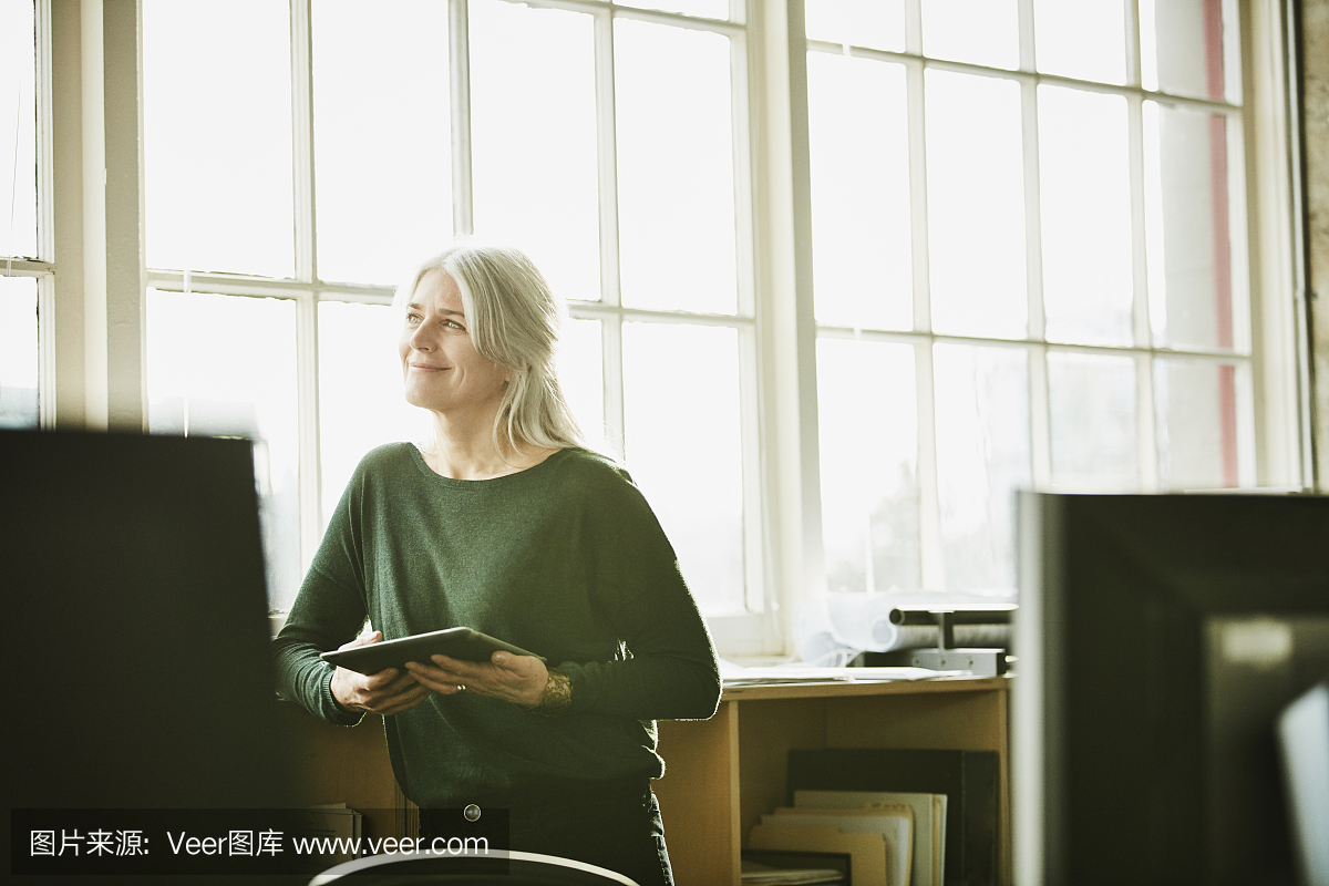 微笑在数字平板电脑在设计办公室工作的女商人