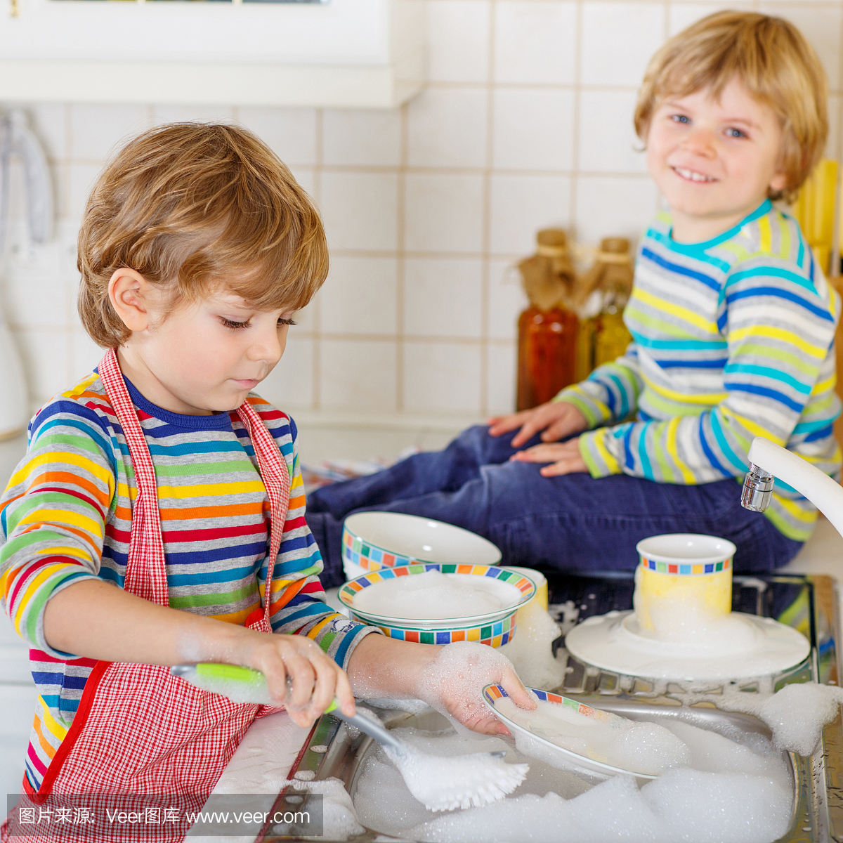 两个小金发双胞胎男孩在家庭厨房里洗碗