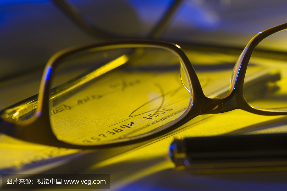 眼镜,笔和支票簿在桌子上,特写镜头,差异焦点