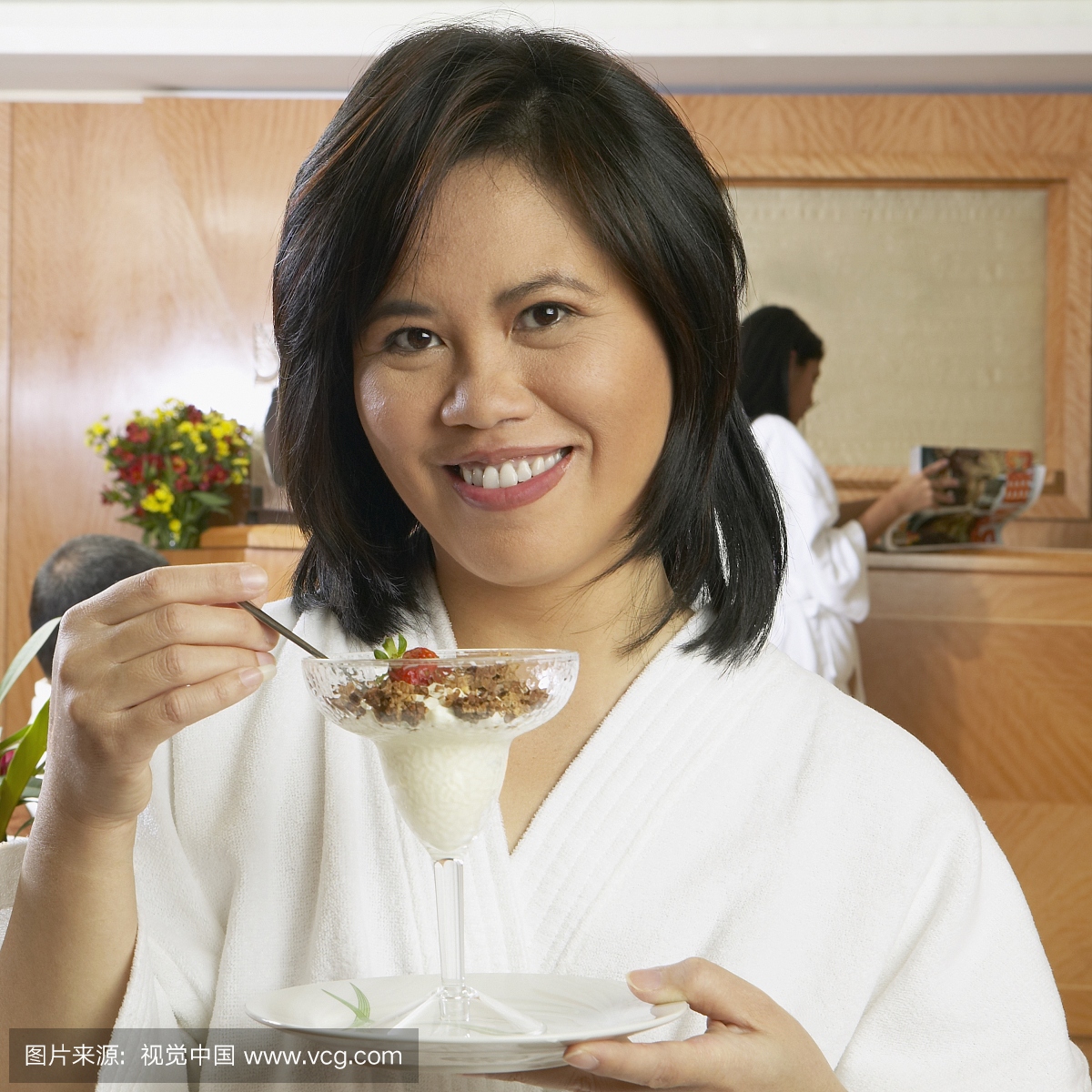 温泉浴袍的亚洲女人在玻璃杯里吃谷物