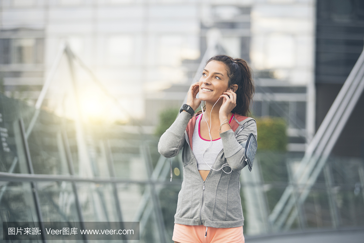 美丽的年轻女子跑步运动员插入她的耳机