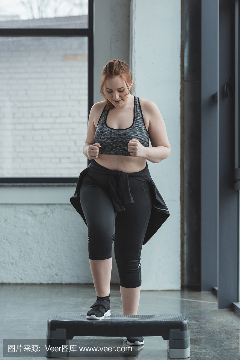 超重女孩在健身房的步骤平台上跳跃