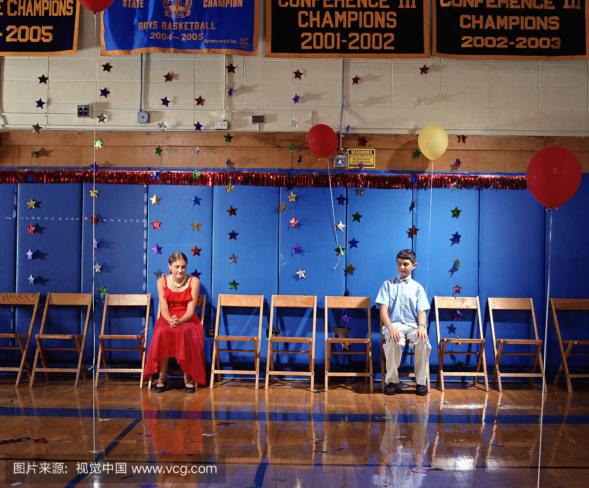 男孩和女孩(11-14)坐在学校舞蹈的健身房墙上