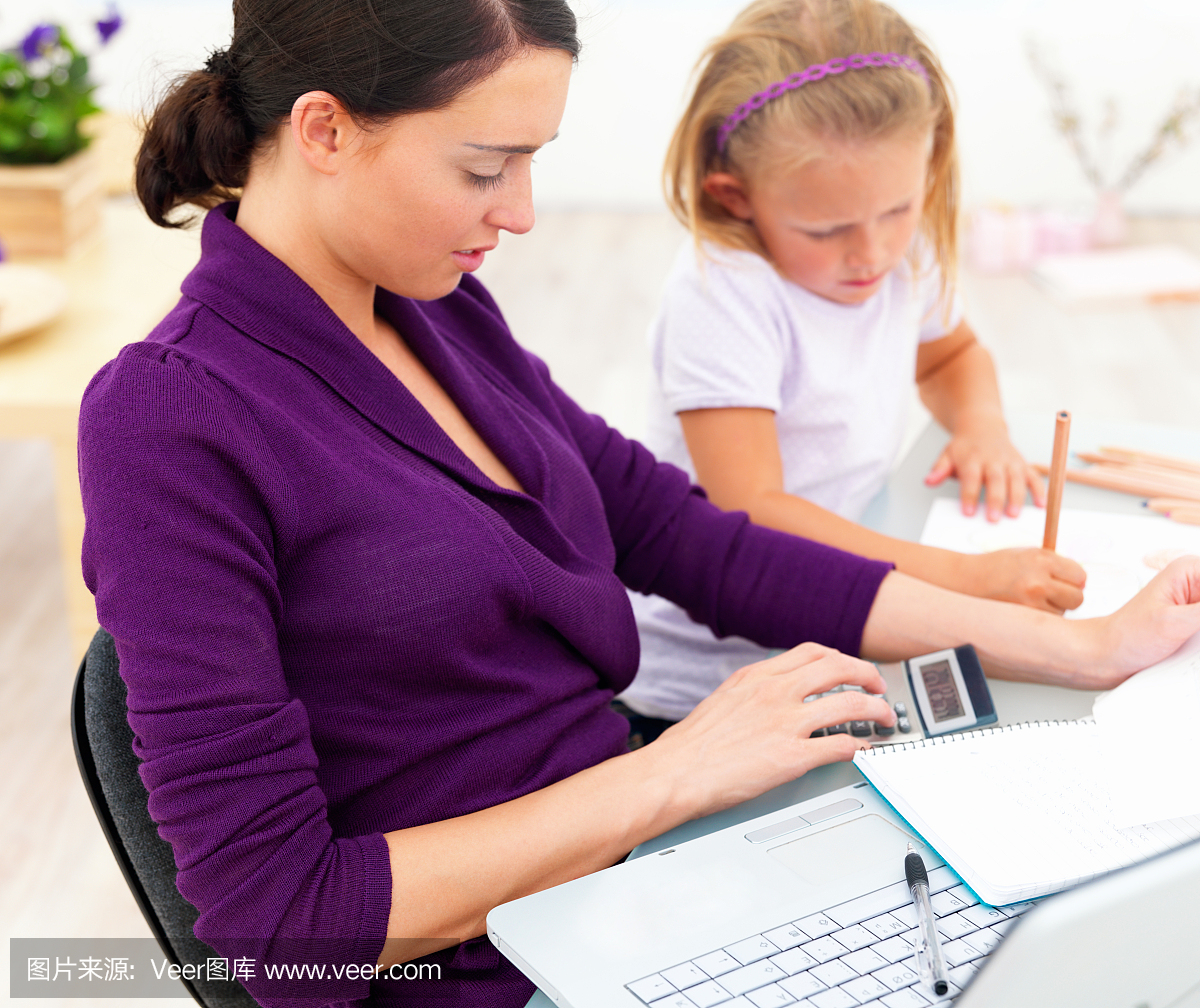母亲和女儿坐在办公桌前用笔记本电脑,文件和