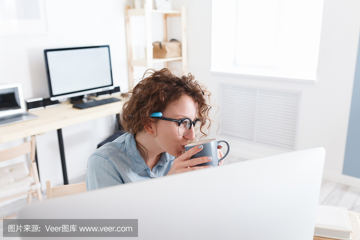 年轻漂亮的女孩设计师坐在电脑前的办公室的桌