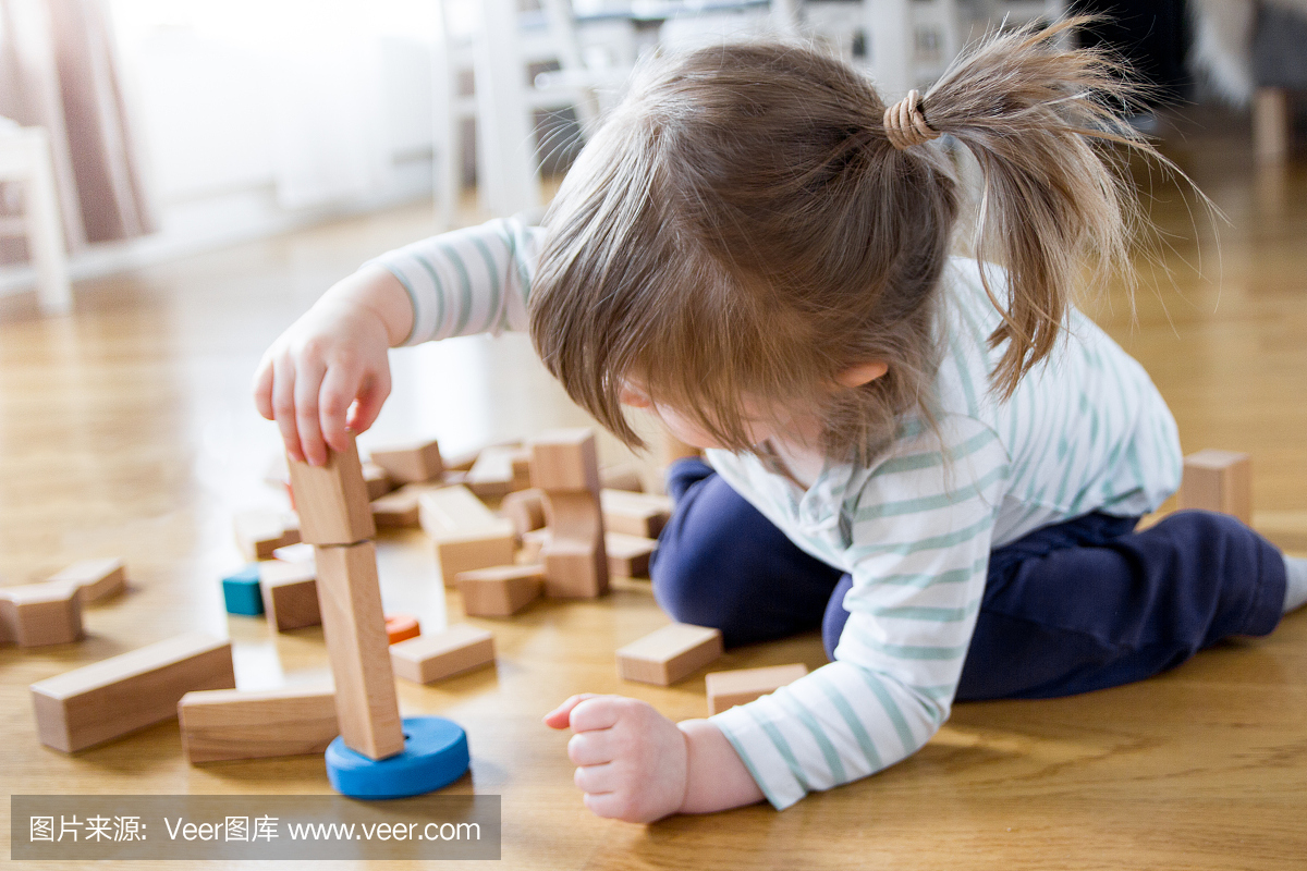 2岁的女孩正在玩和建造一个木制玩具积木塔