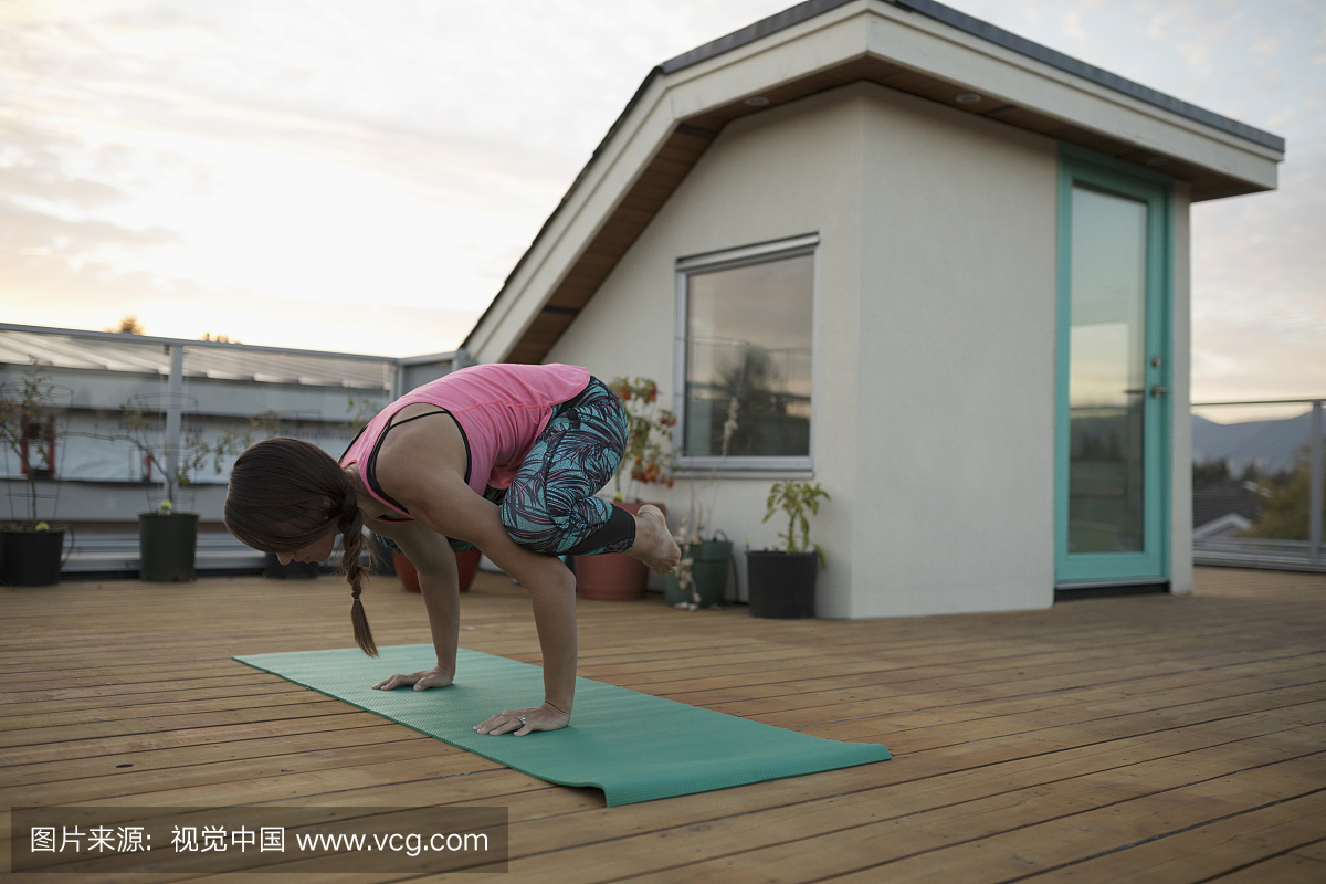 女人练习瑜伽乌鸦摆在露台甲板上的瑜伽垫上