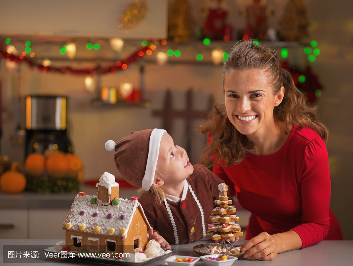 微笑的母亲和婴儿与圣诞饼干的房子在厨房里