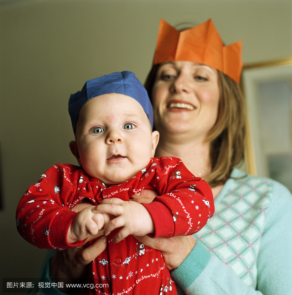 女子抱着男婴(3-6个月),戴着纸帽子