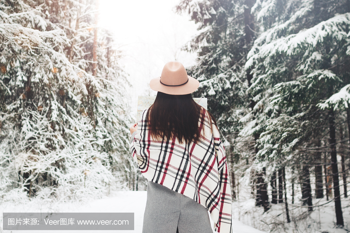 年轻女性时髦旅行在冬季森林中的大雪树在手中