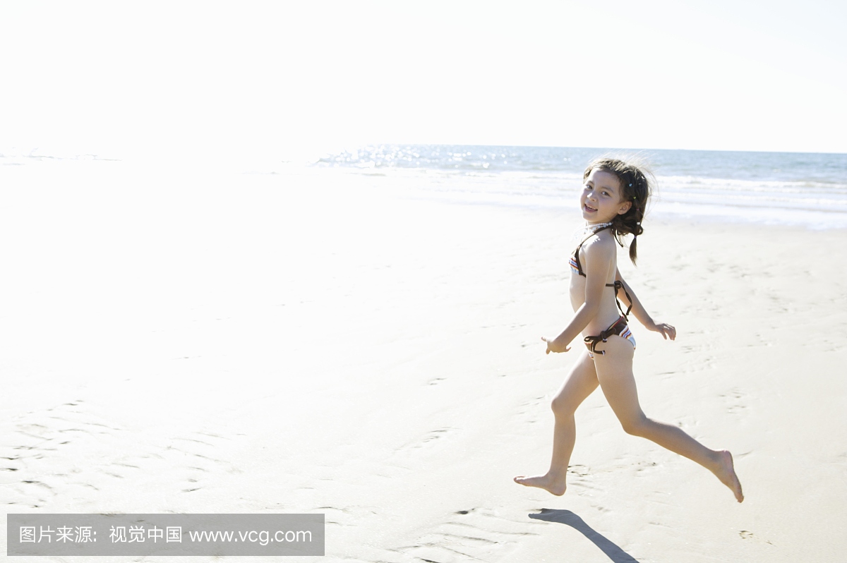美丽的女孩穿比基尼运行在沙滩上看着相机