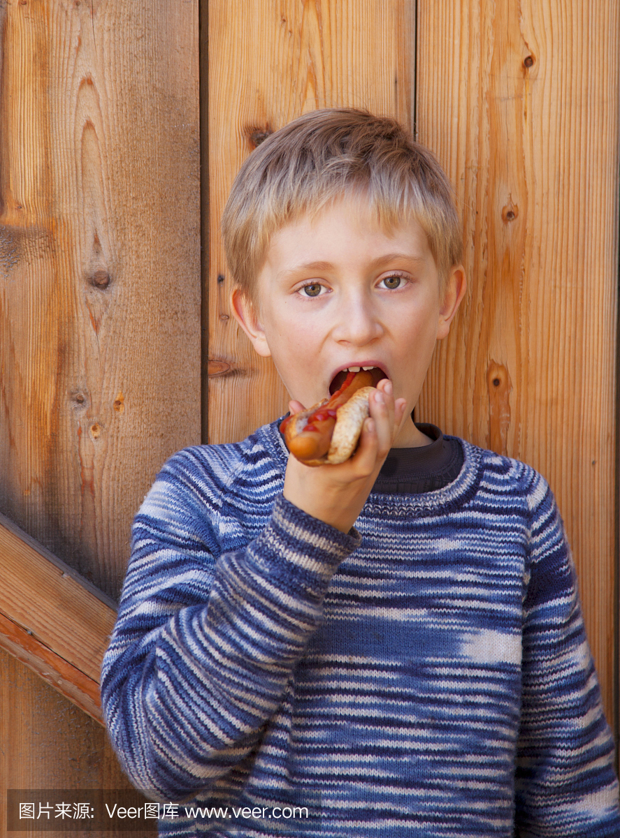 年轻男孩吃热狗对木背景