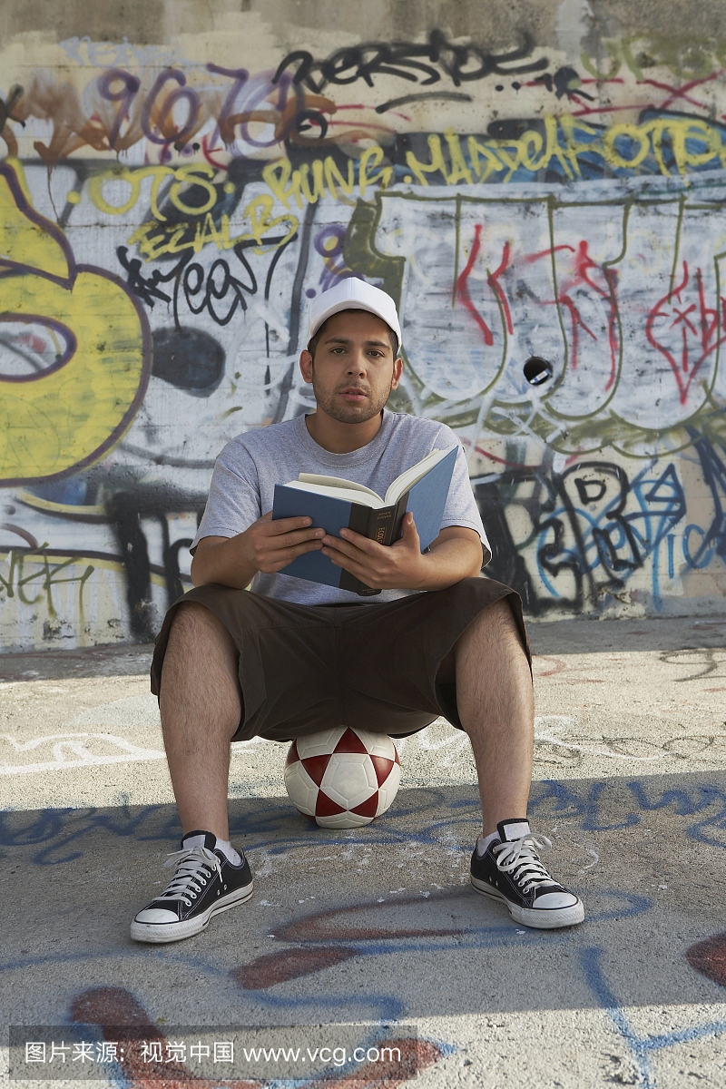 坐在一个足球上拿着一本书的年轻男子的肖像