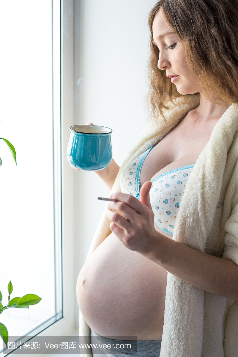 一个怀孕的女人,一个大肚子拿着一杯咖啡和一