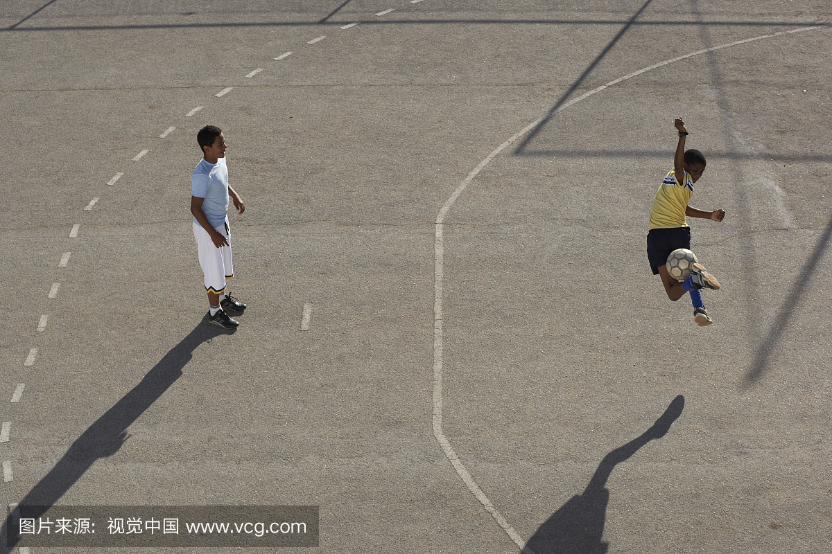 两个男孩(11-13岁)在沥青上踢足球,身高高高